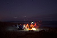 Friends hanging around a beach bonfire lighting the dark night. Original public domain image from Wikimedia Commons