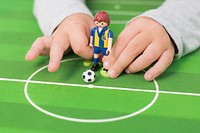 A child plays with a soccer figure on a green table. Original public domain image from Wikimedia Commons