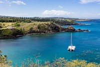 A lone sailboat sitting in a bright blue lagoon along a green forest in Maui. Original public domain image from Wikimedia Commons