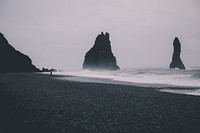 Man standing on a black sand beach on an overcast day. Original public domain image from Wikimedia Commons