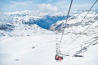 Two people sitting on a chairlift with skis on top of snow covered mountains in Val Thorens. Original public domain image from <a href="https://commons.wikimedia.org/wiki/File:Ski_lift_people_on_snow_mountains_(Unsplash).jpg" target="_blank">Wikimedia Commons</a>