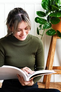 Young woman reading a book about gardening surrounded by potted plants