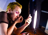 Non-binary person applying eye makeup, using LED ring light, beauty blogger