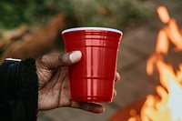 Man carrying a party cup by a fireside