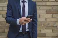 Free close up of man holding a smart phone standing in front of a brick building image, public domain CC0 photo.