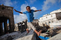 A Somali boy jumps between to old fishing boats above Mogadishu's fishing harbour near the fish market in the Somali capital, 16 March, 2013. Original public domain image from Flickr