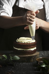 Pastry chef using icing bag to decorate chocolate cake, free public domain CC0 photo.