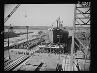 Launching of 10,000 ton ships. The first of 90 sister ships to be built for the Maritime Commission slides off the dock into the Atlantic. Launched just one year from the time construction work started on the shipyards, this 10,000 ton vessel is of the "Virginia Dare" type. In the future these ships will slide down the runway at the rate of one per week. From laying of keel to launching takes only 90 days. Sourced from the Library of Congress.