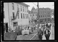 Stock at the Hardwick Victory store overflows at times onto the lawn and even front railing serves as vantage point for display of such items as carpets and mattresses. Reopened May first, the store is again the center of trade in Hardwick. Sourced from the Library of Congress.