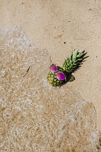 Fresh pineapple with a pink sunglasses lying at the beach