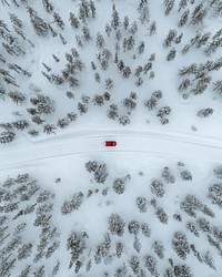 Drone view of a red car driving though a snowy forest in Lapland, Finland