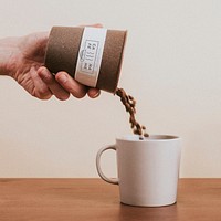 Hand pouring coffee beans into a mug mockup