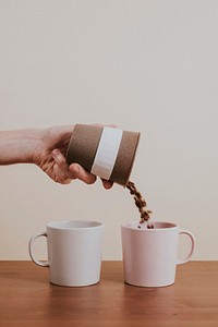 Hand pouring coffee beans into a ceramic mug