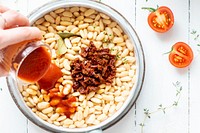 Woman pouring homemade tomato sauce into a pot with beans