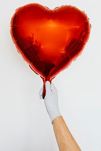 Gloved hand holding a red heart shaped balloon