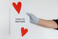 Gloved hand holding a thank you doctors card during the COVID-19 pandemic