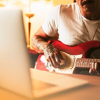 Tattooed man practicing electric guitar at home