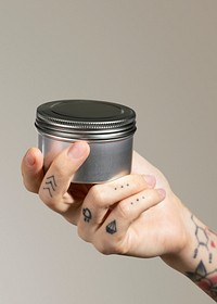 Tattooed hand holding face cream jar