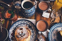 An overhead shot of a breakfast table with pancakes, mugs, drinks, and food. Original public domain image from Wikimedia Commons