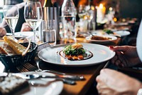 A person sitting over a gourmet meal at a long table with numerous plates and wine glasses. Original public domain image from <a href="https://commons.wikimedia.org/wiki/File:Gourmet_meal_and_white_wine_(Unsplash).jpg" target="_blank" rel="noopener noreferrer nofollow">Wikimedia Commons</a>
