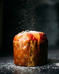 A muffin wrapped in paper and sprinkled with powdered sugar. Original public domain image from Wikimedia Commons