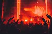 Silhouettes of concert audience raising their hands in the air in front of a stage bathed in red light. Original public domain image from Wikimedia Commons