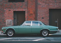 A classic green car is parked in front of a brick building in New York.. Original public domain image from Wikimedia Commons