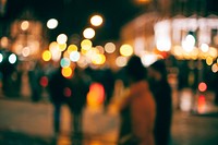 An out-of-focus look at people walking outside in a town at night with with blurs of dotted light all around. Original public domain image from <a href="https://commons.wikimedia.org/wiki/File:Street_bokeh_(Unsplash).jpg" target="_blank" rel="noopener noreferrer nofollow">Wikimedia Commons</a>