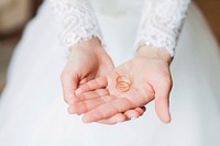 Bride with wedding bands in her hand, with lace wedding dress blurred into the background. Original public domain image from Wikimedia Commons