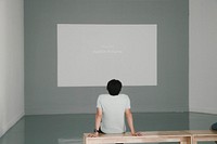 Man sitting on bench watching exhibition film. Original public domain image from <a href="https://commons.wikimedia.org/wiki/File:Man_watches_art_slideshow_(Unsplash).jpg" target="_blank">Wikimedia Commons</a>