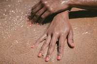 Hands with fingernails painted pink in the wet sand. Original public domain image from Wikimedia Commons