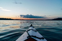 A perspective shot from a kayak on a rippling lake with the sun setting on the horizon in the distance. Original public domain image from Wikimedia Commons