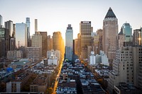 Cityscape with low buildings and tall skyscrapers, the sun's light shining on them in New York City, United States. Original public domain image from Wikimedia Commons