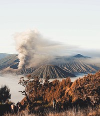 Several people on a mountain slope with a cloud of smoke rising up from a volcano crater in the background. Original public domain image from Wikimedia Commons