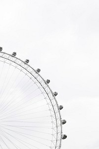 Part of a ferris wheel with enclosed cars for riding in and people in the cars against an overcast sky. Original public domain image from Wikimedia Commons