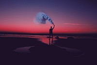 A silhouette of a man holding a smoke bomb on a deserted beach, with a pink sunset sky in the background. Original public domain image from Wikimedia Commons