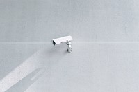 A white surveillance camera casts a shadow on a blank white wall. Original public domain image from Wikimedia Commons