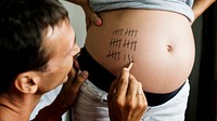 Father marking pregnancy due date on a woman&rsquo;s baby bump