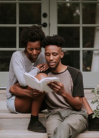 Cute black couple reading a book together in a garden