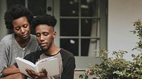 Cute black couple reading a book together in a garden