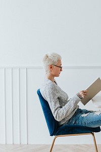 Woman sitting on a blue velvet chair reading a book