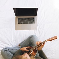 Woman using a laptop while playing ukulele during lockdown