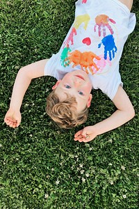 Smiling kindergarten boy lying down on the grass aerial view