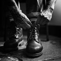 Tattooed man tying boot shoelaces on the floor