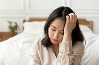 Asian woman sitting sad by her bed