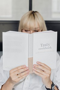Short blond-haired woman reading a book on a gray couch