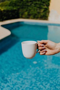 Woman holding a white coffee cup by the pool