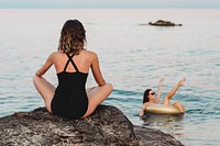 Girl sitting on a rock watching her friend in a gold swim tube