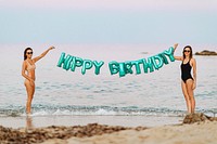 Girls holding a happy birthday foil balloons at the beach