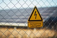 High voltage signboard on a mesh fence with alternative solar panels